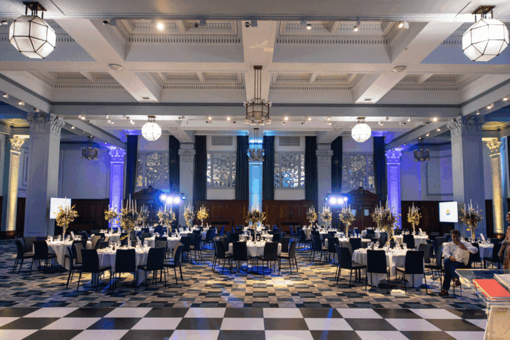 A spacious, elegant banquet hall with checkered floors and high ceilings, decorated with round tables, floral centerpieces, and dramatic lighting—one of the finest Manchester event venues, ready for a formal gathering.